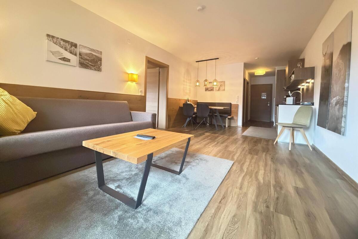 Un salon moderne avec un canapé, une table basse en bois et un coin repas agrémenté d’un piano.