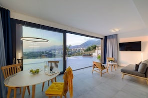 Una sala de estar moderna con un gran ventanal que da a un balcón, un comedor con mesa y sillas, y un sofá.