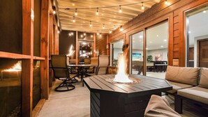 A cozy outdoor patio with a fire feature, wooden walls, and a glass door leading to an indoor area.