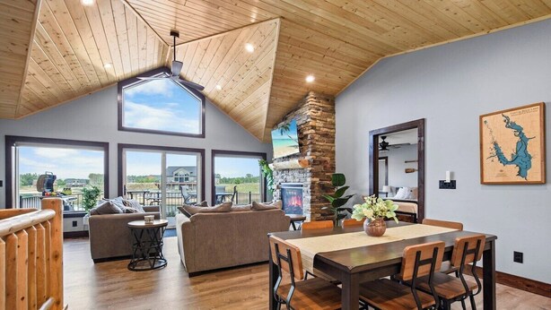 A spacious living area with a high ceiling, large windows, a fireplace, and a dining table.