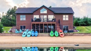 A two-story house with a balcony, a pool, and several kayaks lined up in front.