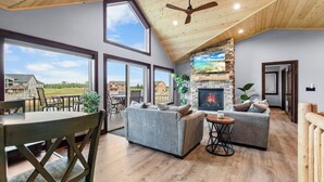 A spacious living room with a stone fireplace, large windows, and a high ceiling.