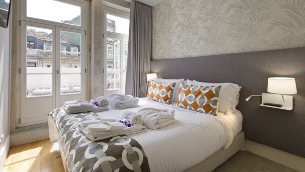 Une chambre d’hôtel avec un lit, des serviettes, une lampe fixée au mur et une fenêtre avec des rideaux.