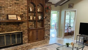 A living room with a brick fireplace, wooden shelves, a glass coffee table, and a television.