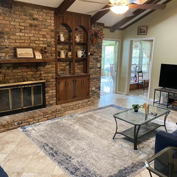 A living room with a brick fireplace, wooden shelves, a glass coffee table, and a television.