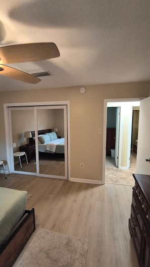 A spacious bedroom with a large sliding door leading to a bathroom, a ceiling fan, and a wooden dresser.
