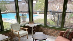 A sunlit room with a pool view, a cushioned sofa, a chair, a small table, and a decorative rug.