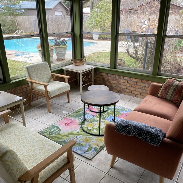 Une pièce lumineuse donnant sur la piscine, avec un canapé confortable, un fauteuil, une petite table et un tapis décoratif.