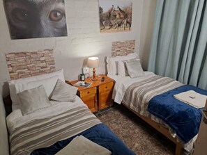 Two single beds with striped bedspreads and pillows, a nightstand with a lamp and table, and a large giraffe poster adorn this cozy space.