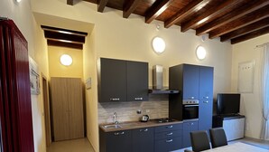A modern kitchen with dark cabinets, a wooden ceiling, and a dining area with a table and chairs. - In Centro - Rooms and Apartments  (Isola del Liri)