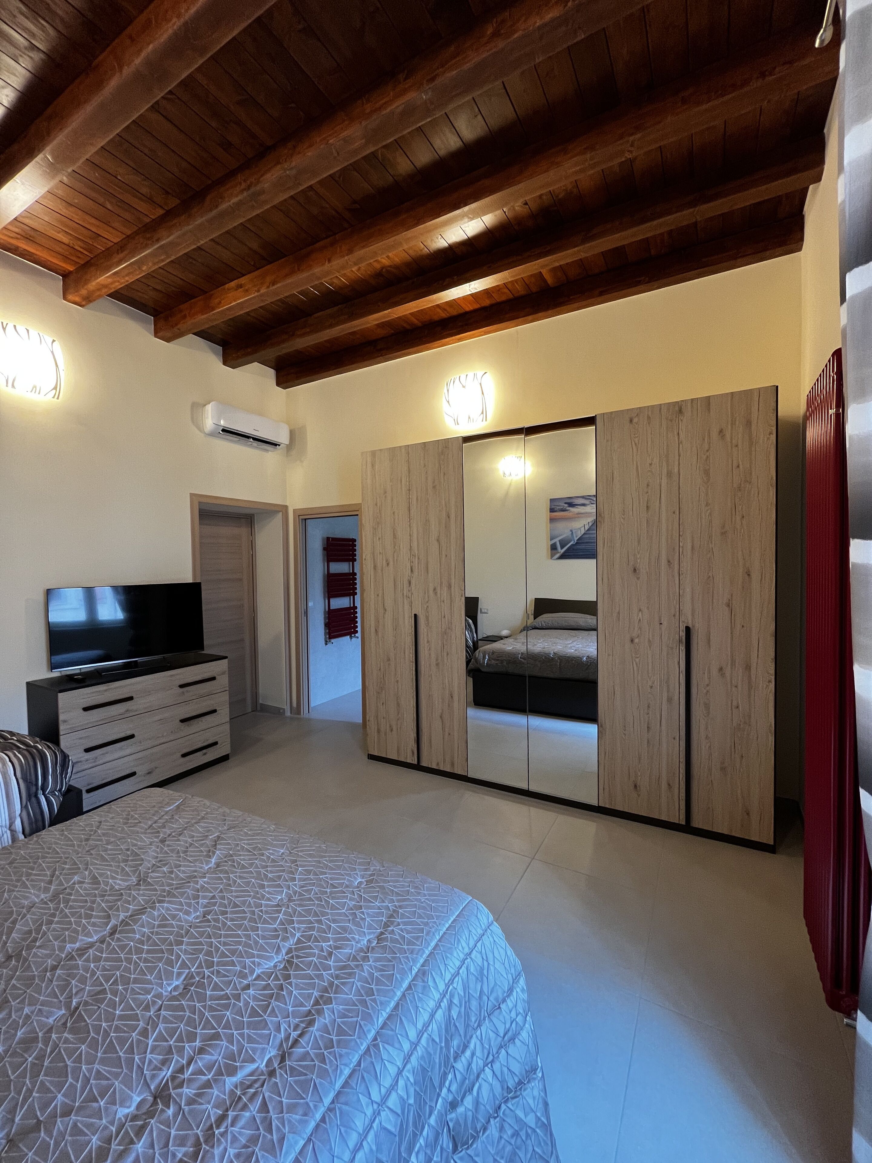 A bedroom with a bed, a TV, a wardrobe, and a mirror.