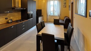 A modern kitchen with dark cabinetry, a central island, and a dining area with a large table and chairs. - In Centro - Rooms and Apartments  (Isola del Liri)