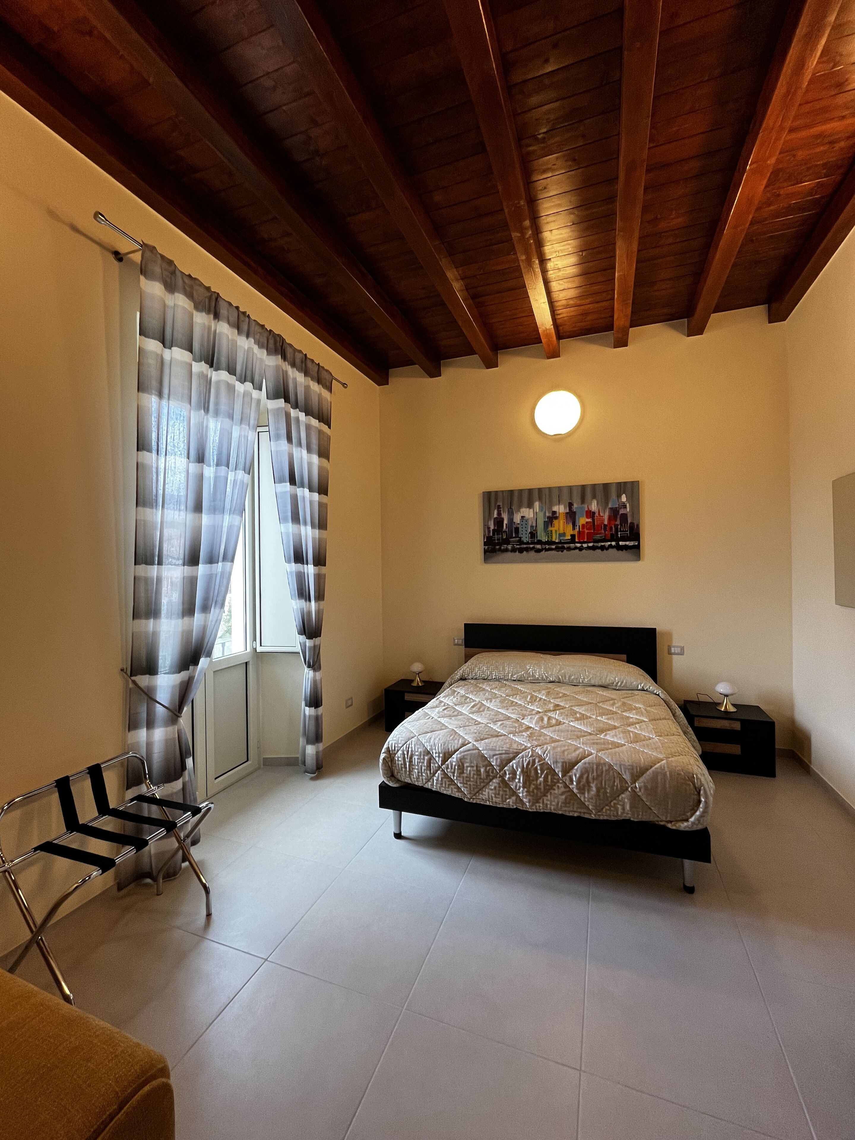 Une chambre à coucher avec un lit, une table de chevet, une chaise, une fenêtre avec des rideaux et un tableau au mur.