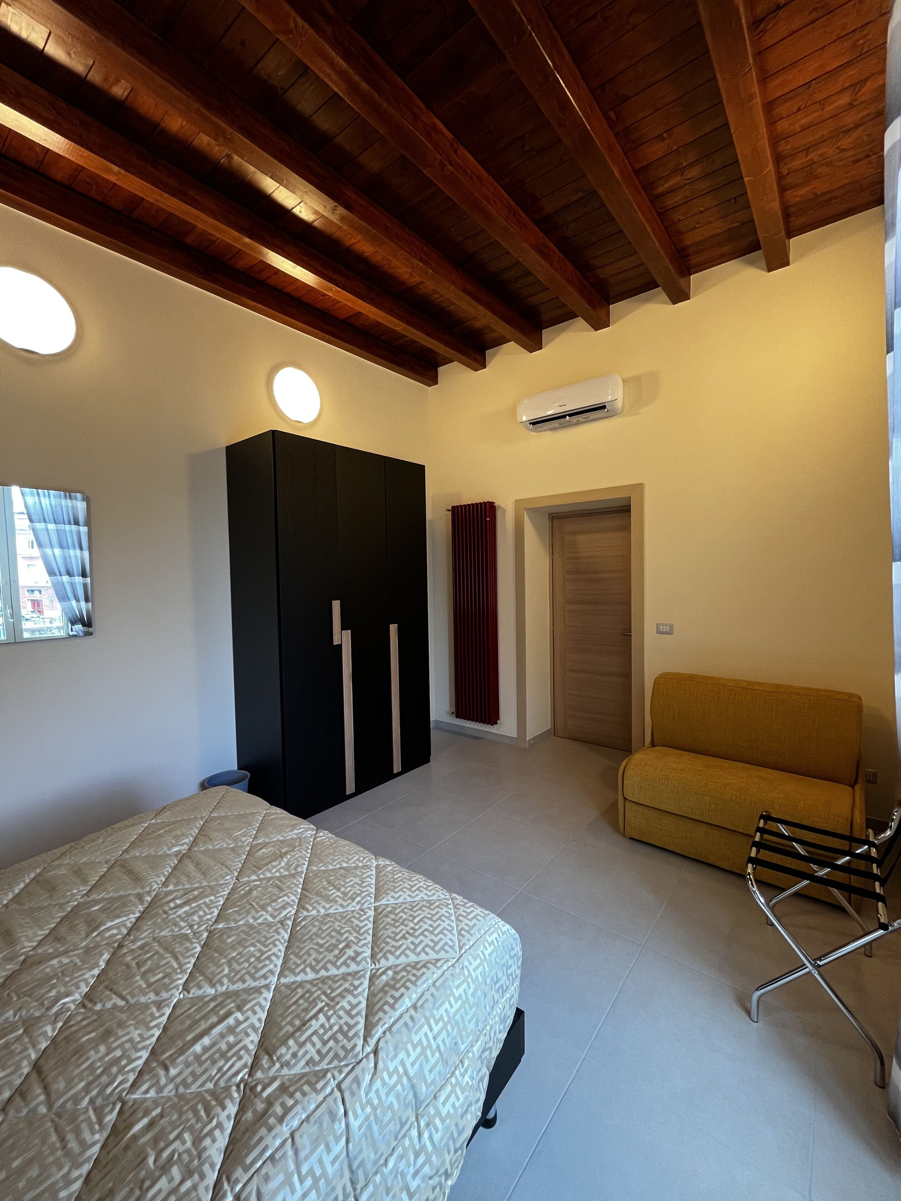 A bedroom with a bed, a wardrobe, a sofa, and an air conditioning unit.