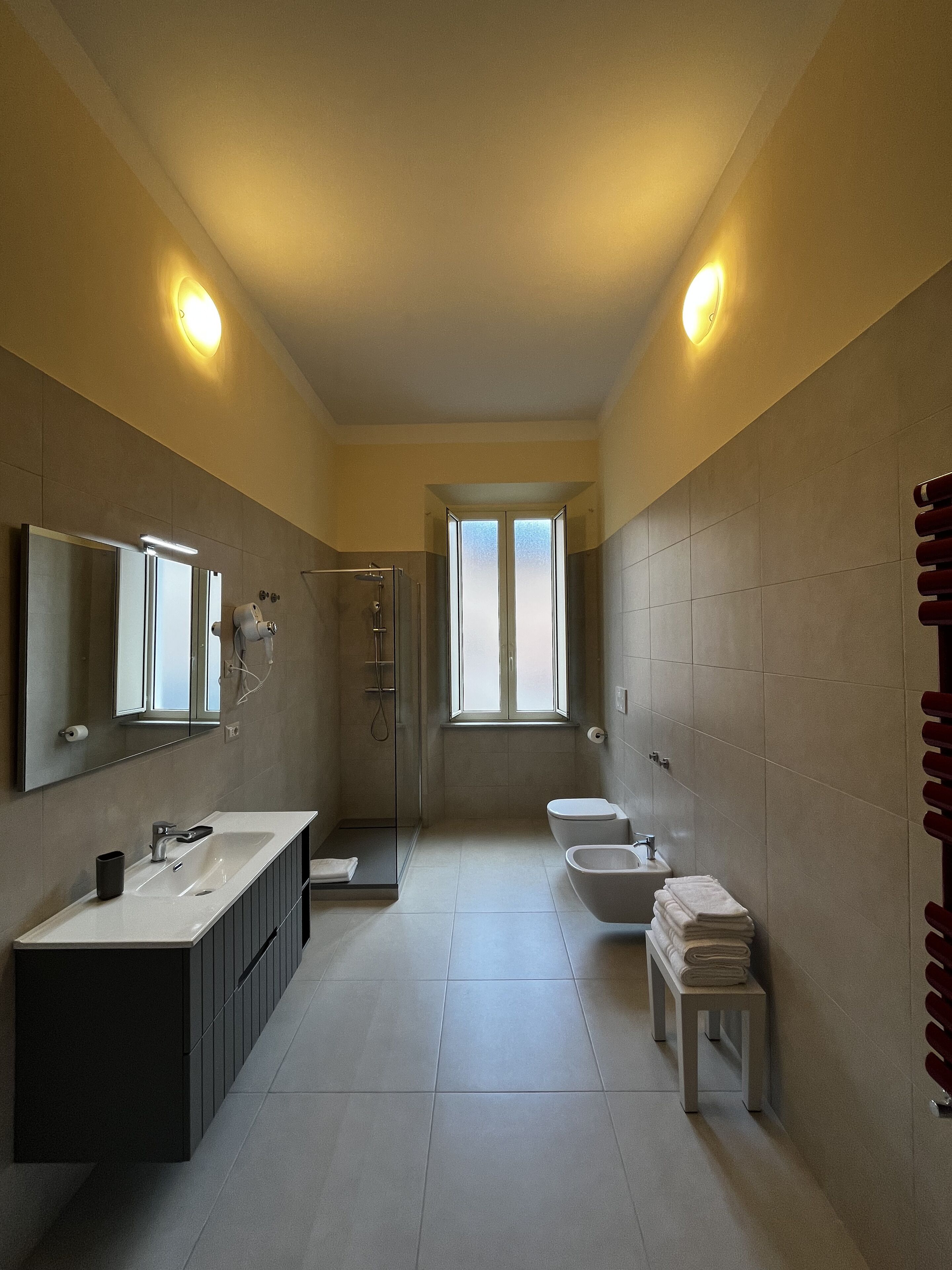 Een moderne badkamer met een grote spiegel, twee wastafels, een douche en een toilet.