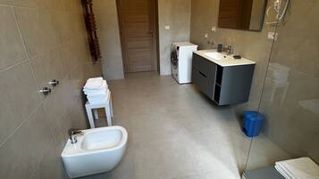 A modern bathroom with a toilet, bidet, sink, and mirror.
