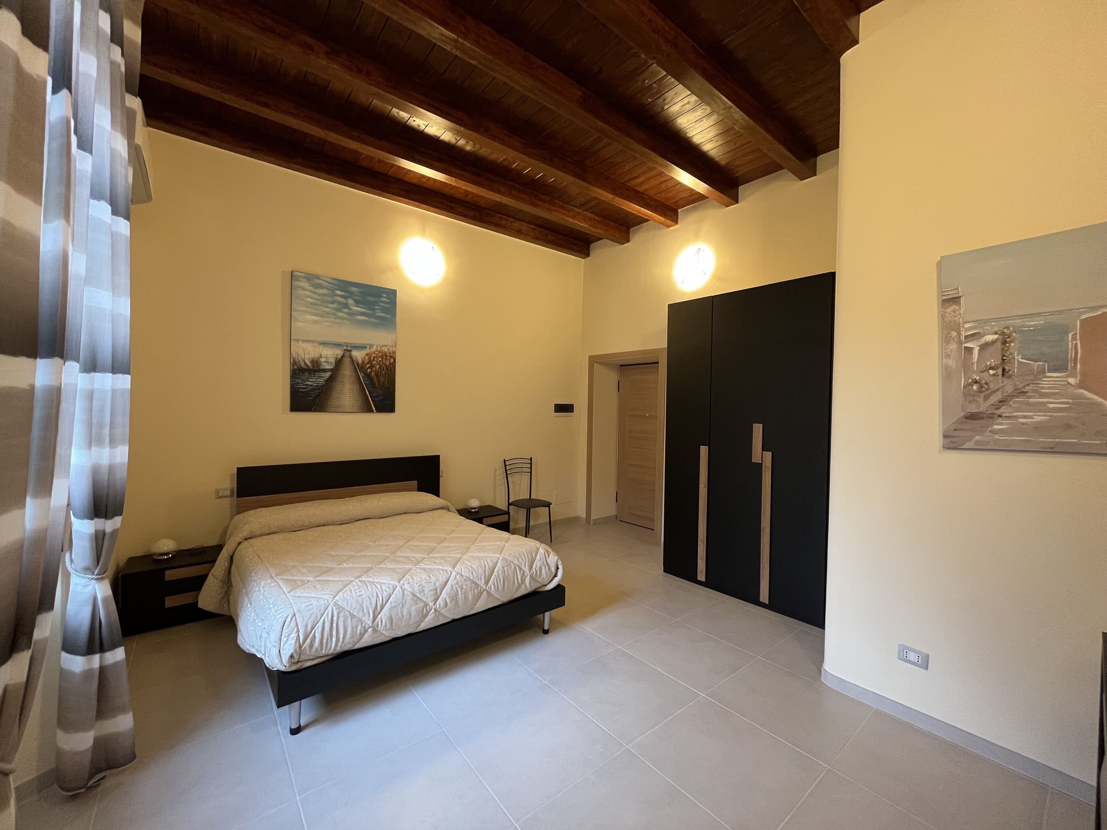 A bedroom with a bed, a nightstand, a chair, a wardrobe, and two paintings on the walls.