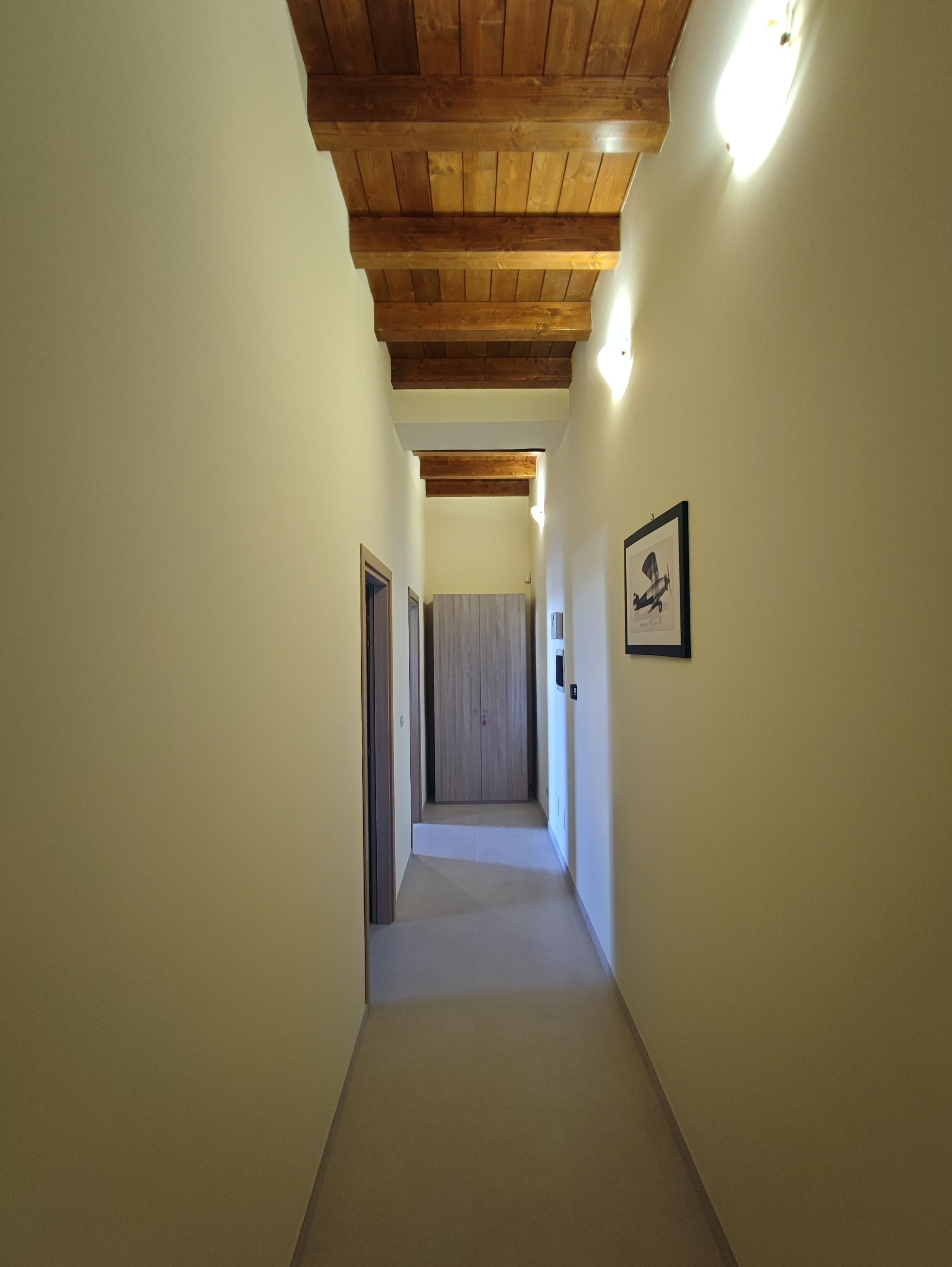 Un couloir étroit avec des poutres en bois au plafond et un tableau encadré au mur.