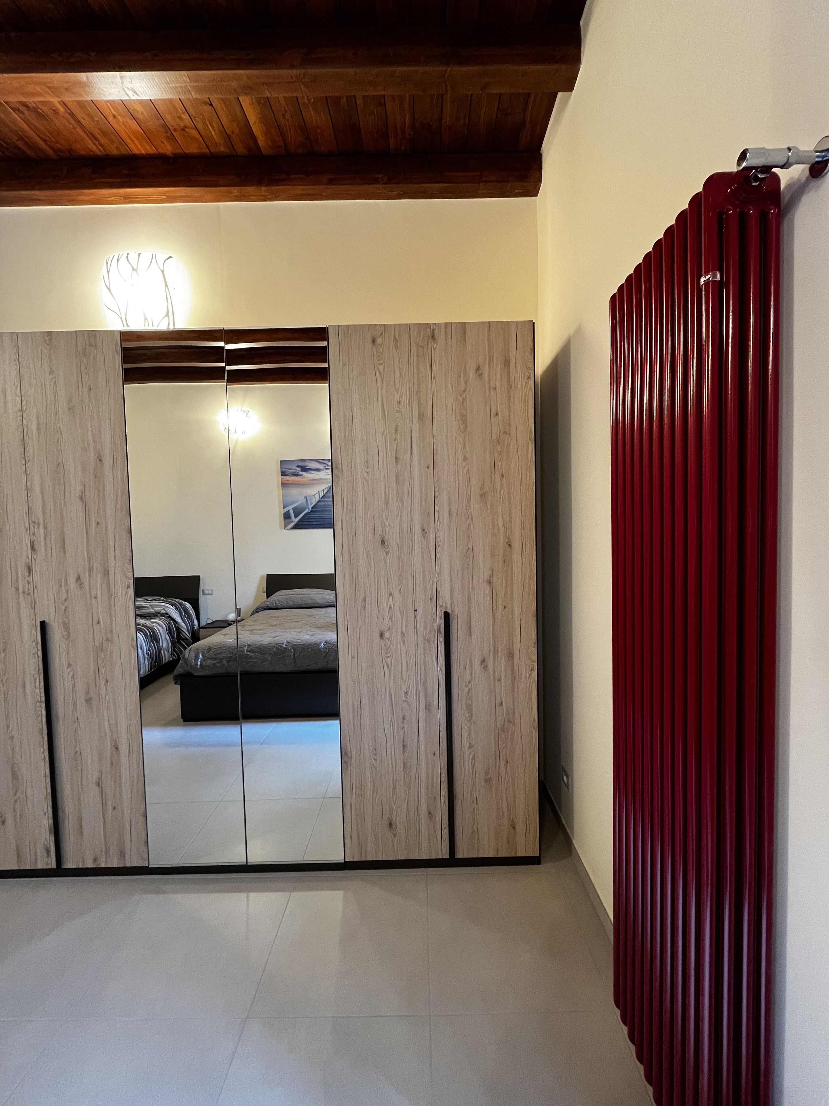 A room with a wooden ceiling, a bed with a striped bedspread, and a red radiator.
