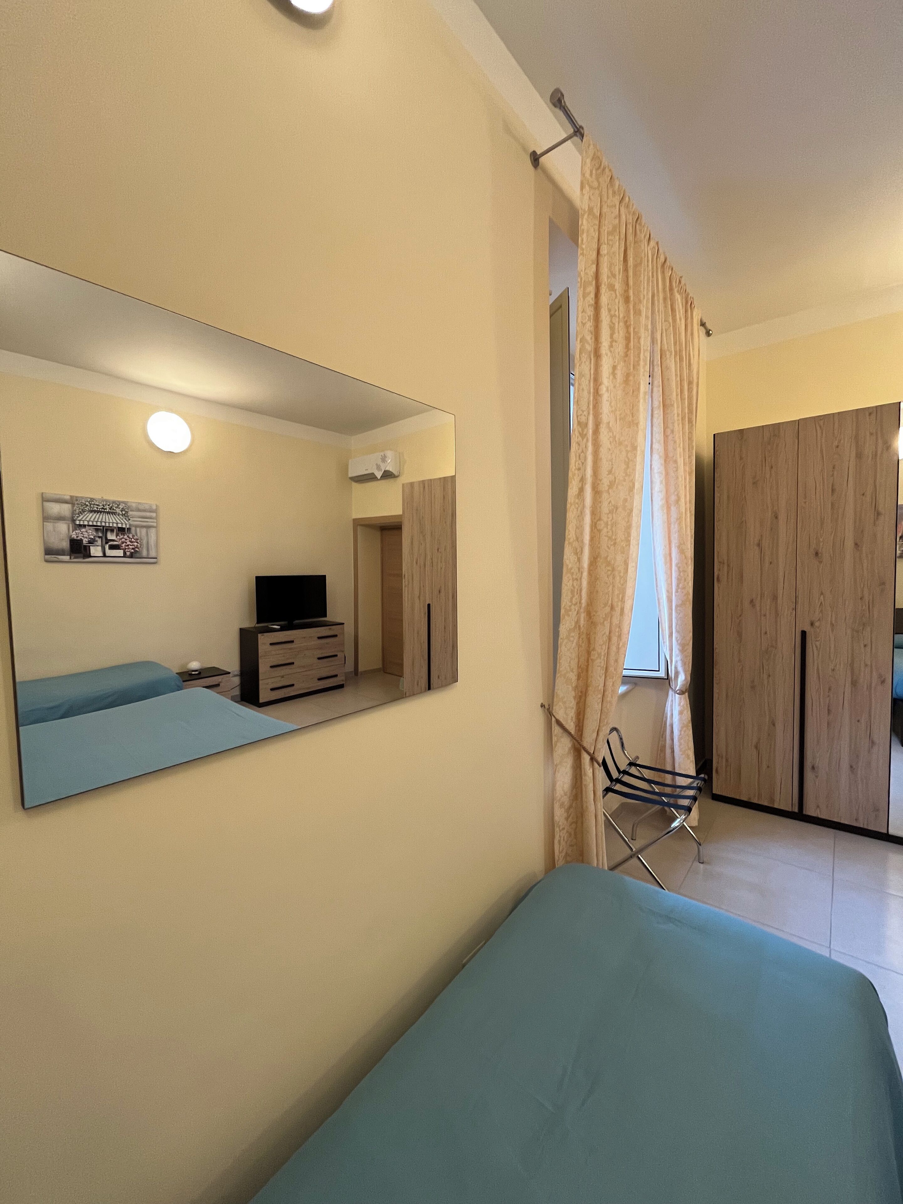 Een slaapkamer met een bed, een dressoir, een televisie, een spiegel en een kledingkast.