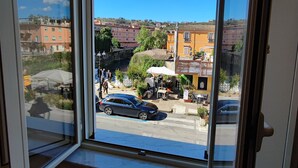 A view from a room with a large window overlooking a street with parked cars and buildings. - In Centro - Rooms and Apartments  (Isola del Liri)