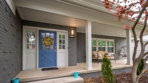 A house with a blue front door, a porch with a bench, and a small tree. - Beautiful Spacious Home- Near the Expo, TU, gathering Place, Fair park (Tulsa)