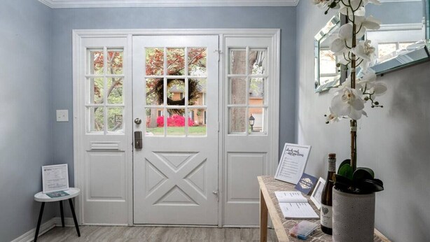 A room with a white door with glass panels, a small table with papers, a potted plant, and a wall-mounted mirror. - Beautiful Spacious Home- Near the Expo, TU, gathering Place, Fair park (Tulsa)