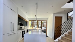 A modern kitchen with a central island, wooden flooring, and a staircase with a black railing. - Live/Work House w/Views, Yard, Parking 3br/2ba (San Francisco)