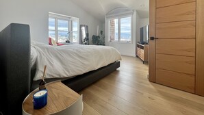 A modern bedroom with a large bed, a TV, and a city view through the windows. - Live/Work House w/Views, Yard, Parking 3br/2ba (San Francisco)