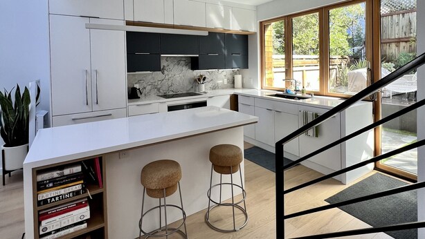 A modern kitchen with white cabinetry, a marble backsplash, and a large island with stools. - Live/Work House w/Views, Yard, Parking 3br/2ba (San Francisco)