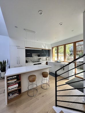 A modern kitchen with white cabinetry, a marble backsplash, and a large island with stools.