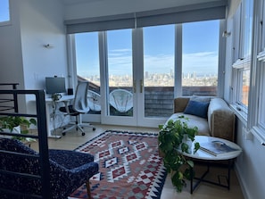 A modern living room with a city view, a desk with a computer, and comfortable seating.