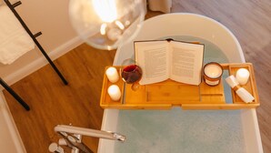 Una bandeja de madera con velas, un libro y una copa de vino tinto en una bañera.