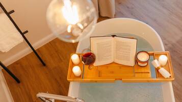 Ein hölzernes Tablett mit Kerzen, einem Buch und einem Glas Rotwein auf einer Badewanne.