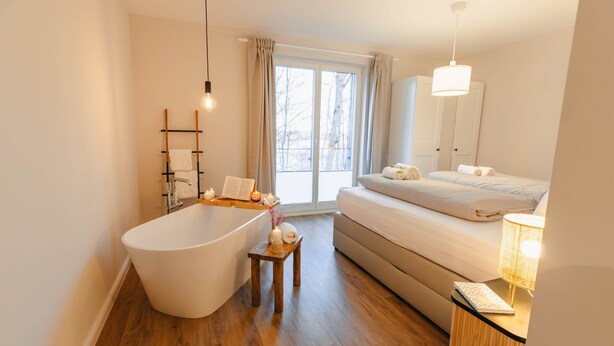 Un baño moderno con una bañera independiente, un tocador de madera y una mesita de noche con lámpara.