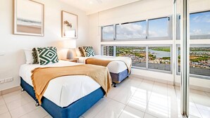 A modern hotel room with two beds, large windows with a city view, and a ceiling fan. - Zen Sea View 2BR, 2BA Penthouse (Darwin City)