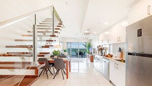 A modern kitchen with a stainless steel refrigerator, a dining area with a table and chairs, and a staircase with wooden steps. - Zen Sea View 2BR, 2BA Penthouse (Darwin City)