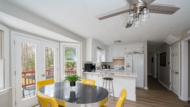 Een moderne keuken met witte kasten, een centraal eiland en een eethoek met gele stoelen.