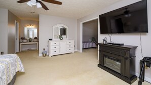 Een slaapkamer met een bed, een dressoir, een televisie en een plafondventilator.