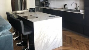 A modern kitchen with a marble island, black bar stools, and stainless steel appliances.