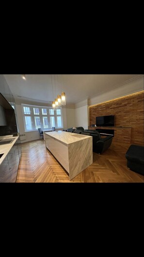 A modern kitchen with a marble island, wooden flooring, and a built-in TV on a brick wall. - Beautiful Heart of Old Town apartment.  (Torun)