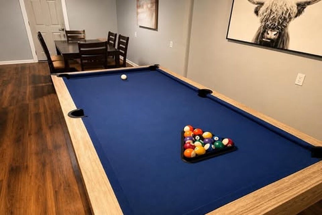 A pool table with balls and a dining area with chairs and a table.