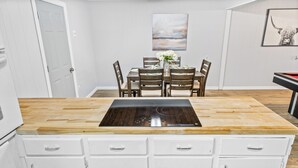Una cocina con encimera de madera, armarios blancos, una zona de comedor con mesa y sillas, y un cuadro en la pared.