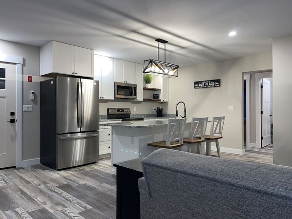 A modern kitchen with stainless steel appliances, a central island, and a dining area with chairs.