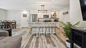 Una cocina moderna con armarios blancos, una isla central con taburetes y un comedor con mesa y sillas de madera.