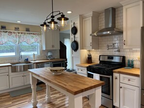A modern kitchen with white cabinetry, a wooden countertop, a stainless steel stove, and a hanging pot rack. - Perfect In-Town Bungalow (Charlevoix)