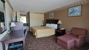 A hotel room with a bed, desk, chair, and a painting on the wall. - Countryside Inn & Suites (Idabel)