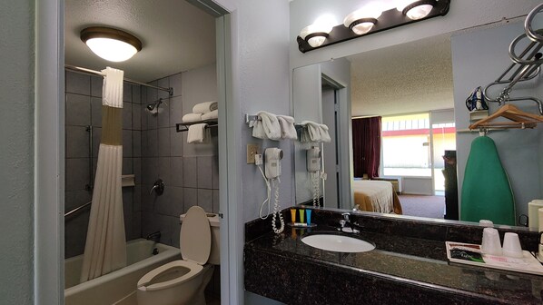 A bathroom with a toilet, sink, and shower. There are towels hanging on the wall and a hairdryer.