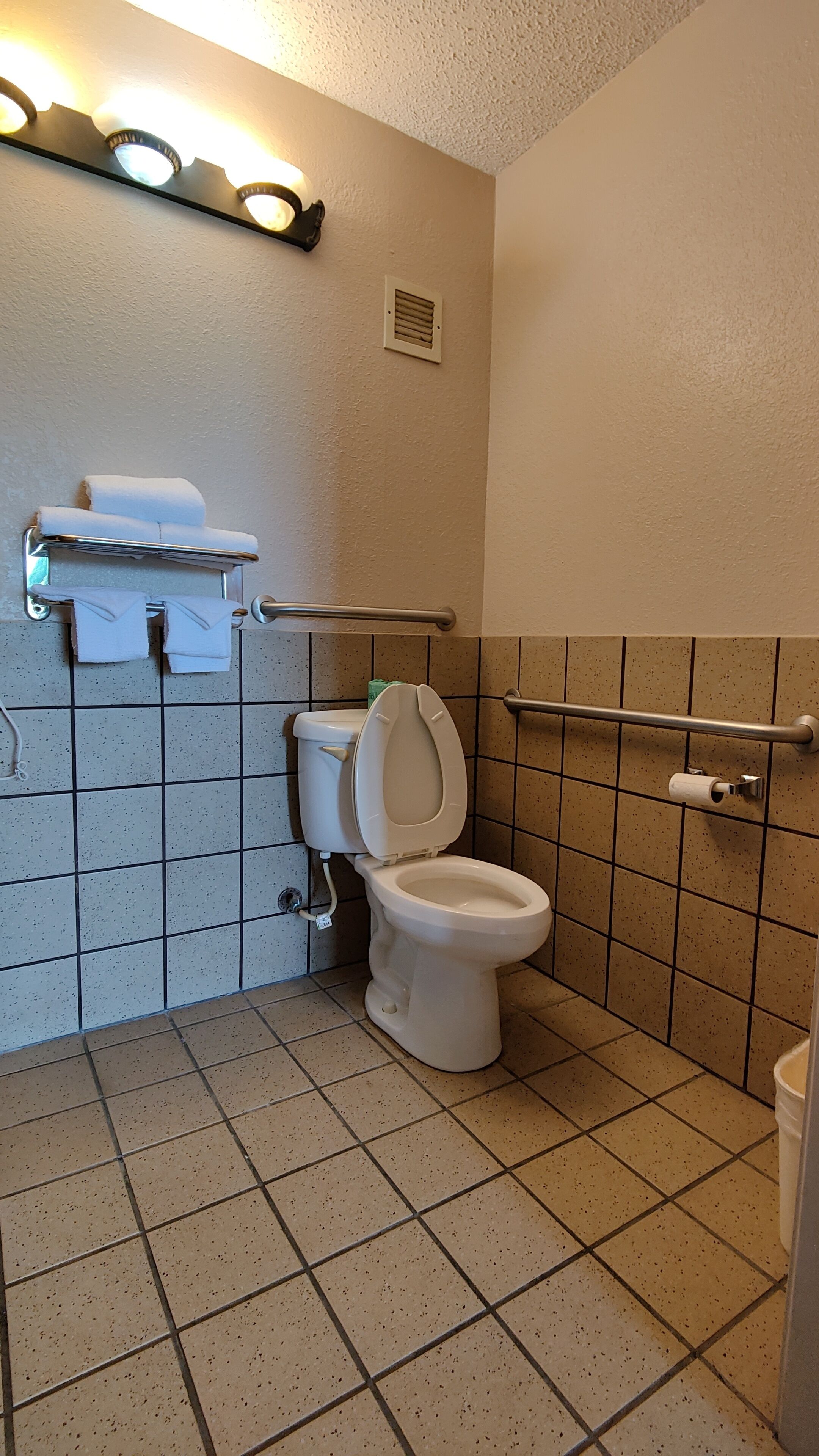 Une petite salle de bain propre, équipée de toilettes, d’un sèche-mains et d’un porte-serviettes.
