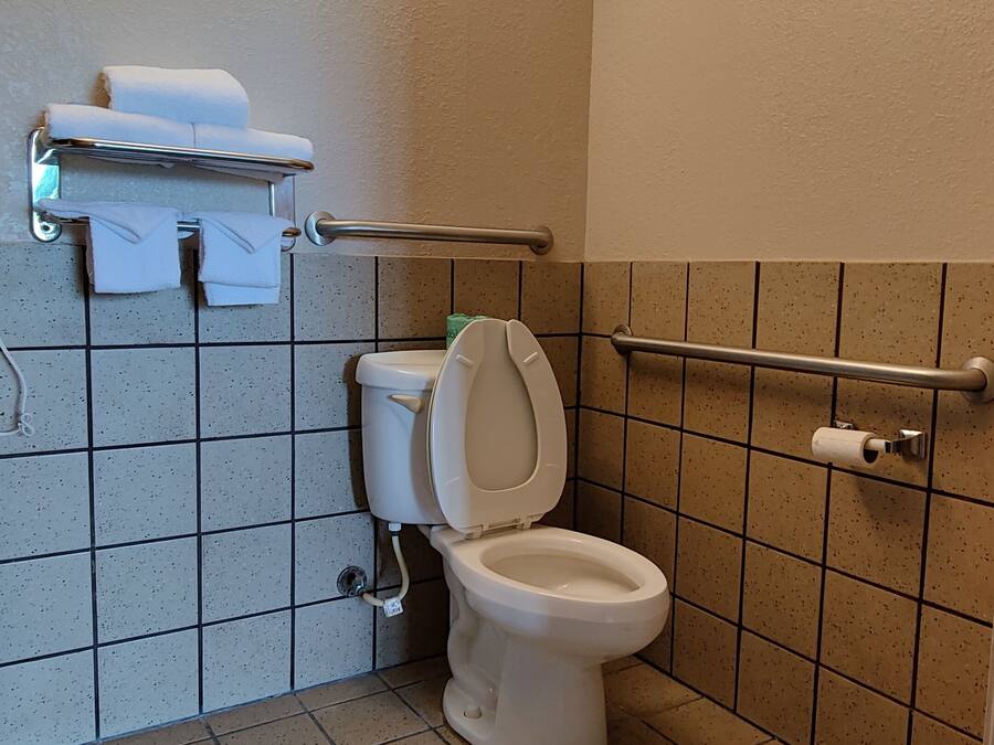 Une petite salle de bain propre, équipée de toilettes, d’un sèche-mains et d’un porte-serviettes.